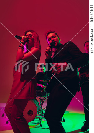 Young caucasian musicians, singers performing in neon light on red studio background 63685611