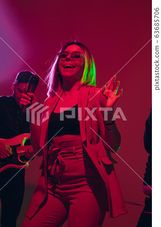 Young caucasian musician, singer performing in neon light on red studio background 63685706