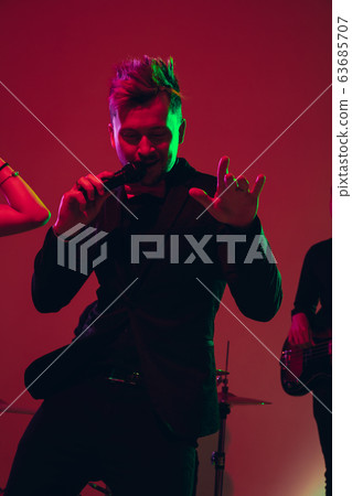Young caucasian musician, singer performing in neon light on red studio background Young caucasian musician, singer performing in neon light on red studio background 63685707