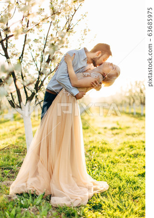 Beautiful, cheerful and romantic couple in love posing in blossoming garden. Handsome man kissing neck of his pretty woman in elegant dress with big passion and love. Spring wedding portrait 63685975