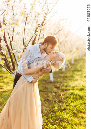 Beautiful, cheerful and romantic couple in love posing in blossoming garden. Handsome man kissing neck of his pretty woman in elegant dress with big passion and love. Spring wedding portrait 63685976