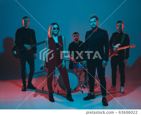 Young caucasian musicians, band performing in neon light on blue studio background Young caucasian musicians, band performing in neon light on blue studio background 63686022