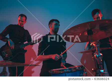 Young caucasian musicians, band performing in neon light on blue studio background 63686024