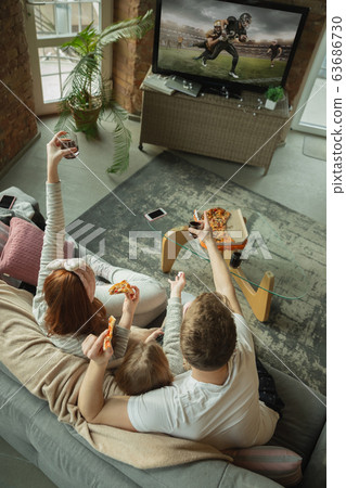 Family spending nice time together at home, looks happy and excited, eating pizza, watching football match Family spending nice time together at home, looks happy and excited, eating pizza, watching football match 63686730