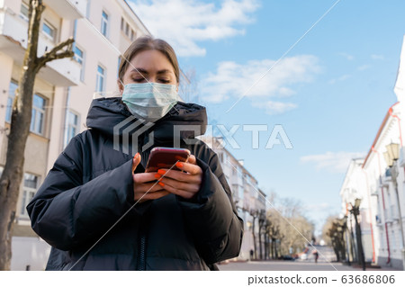 Pportrait of woman in protective medical mask using smart phone on empty european streets. Health and safety, N1H1 coronavirus, covid-19, virus protection care and medical concept. Pan left shot. 63686806
