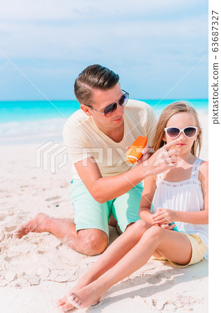 Young father applying sun cream to daughter Young father applying sun cream to daughter 63687327