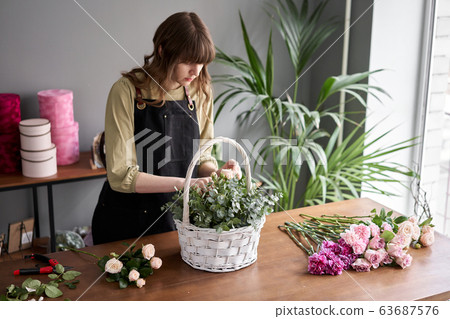 Floral shop concept . Florist woman creates flower arrangement in a wicker basket. Beautiful bouquet of mixed flowers. Handsome fresh bunch. Flowers delivery. 63687576