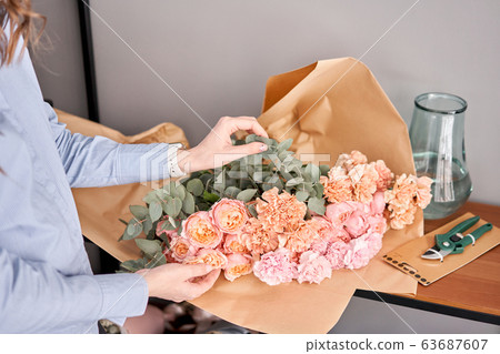 Woman unpack flower set on wooden table. Fresh cut flowers for decoration home. Delivery flower. Woman unpack flower set on wooden table. Fresh cut flowers for decoration home. Delivery flower. 63687607
