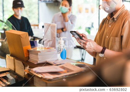 Women in protective face mask placing an order with cell phone at cafe counter. 63692802
