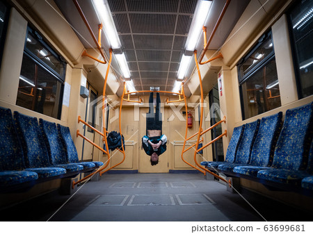 Girl hanging by feet upside down in the subway carriage and using smartphone. Concept of overusing social networks and addiction Girl hanging by feet upside down in the subway carriage and using smartphone. Concept of overusing social networks and addiction 63699681