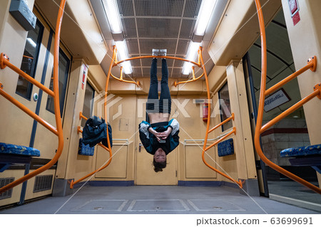 Girl hanging by feet upside down in the subway carriage and using smartphone. Concept of overusing social networks and addiction Girl hanging by feet upside down in the subway carriage and using smartphone. Concept of overusing social networks and addiction 63699691