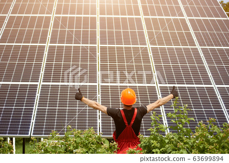 Guy stands with his back to camera against the background of large plantation solar batteries showing thumbs signs like Guy stands with his back to camera against the background of large plantation solar batteries showing thumbs signs like 63699894