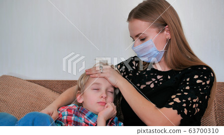 A caring mother in a bandage measures the temperature of her son. A caring mother in a bandage measures the temperature of her son. 63700310