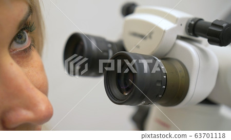 Doctor used microscope. Dentist is treating patient in modern dental office. Operation is carried out using cofferdam. 63701118