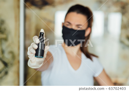 A girl in a protective mask, glasses and gloves spray an antiseptic to prevent infection. 63702403