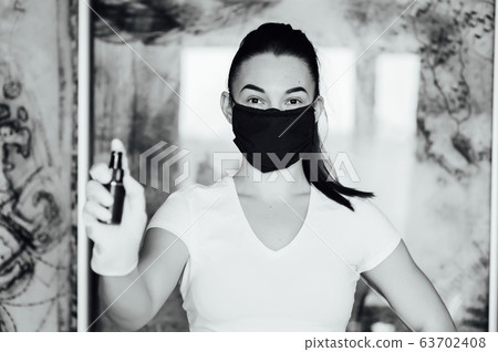 A girl in a protective mask, glasses and gloves spray an antiseptic to prevent infection. 63702408