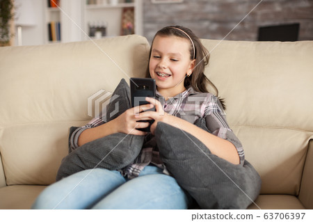 Teen girl with braces sitting on the couch in living room Teen girl with braces sitting on the couch in living room 63706397