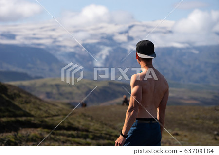 Backside of tall muscular caucasian man with naked torso standing in over mountain and sky background. Promoting active, sport and healthy lifestyle 63709184