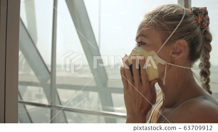 Woman caucasian at airport with wearing protective medical mask on head against the background of the plane. Coronavirus sars-cov-2 covid-19. 63709912
