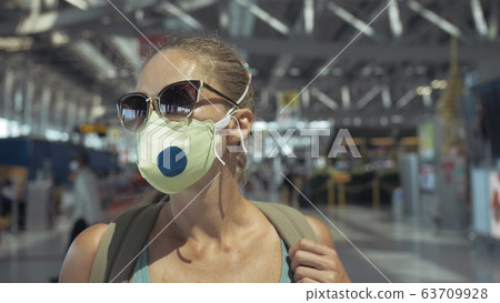 Woman caucasian at airport with wearing protective medical mask on head against the background of the plane. Coronavirus sars-cov-2 covid-19. Woman caucasian at airport with wearing protective medical mask on head against the background of the plane. Coronavirus sars-cov-2 covid-19. 63709928