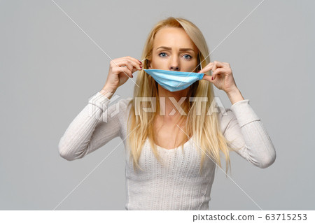 Studio portrait of young woman wearing a face protective mask isolated on gray background - flu virus epidemic protection, dust or pollen allergy, air pollution 63715253