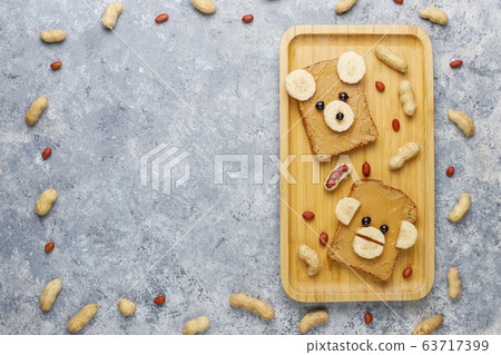 Funny bear and monkey face sandwich with peanut butter, banana and black currant,peanuts on grey concrete background,top view Funny bear and monkey face sandwich with peanut butter, banana and black currant,peanuts on grey concrete background,top view 63717399