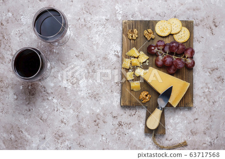 cheese board with hard cheese ,cheese knife,red wine glass,grape on brown concrete background 63717568