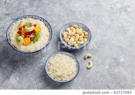 Bowl of rice flakes porridge with kiwi slices,pomegranate seeds,cumquats and cashew nuts on grey concrete background,top view Bowl of rice flakes porridge with kiwi slices,pomegranate seeds,cumquats and cashew nuts on grey concrete background,top view 63717995