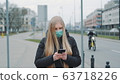Coronavirus pandemic: blonde woman in a medical mask writing message on smartphone 63718226