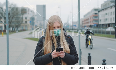 Coronavirus pandemic: blonde woman in a medical mask writing message on smartphone Coronavirus pandemic: blonde woman in a medical mask writing message on smartphone 63718226