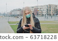 Young female wearing medical mask reading outbreaking news about coronavirus disease on the street 63718228