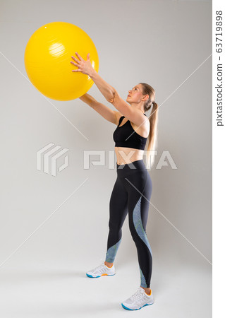 slim fit blonde girl in a sports uniform is engaged in physical exercises on a gray background 63719898