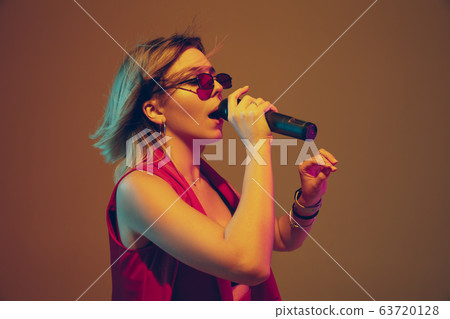 Young caucasian female musician, performer singing, dancing in neon light on gradient background Young caucasian female musician, performer singing, dancing in neon light on gradient background 63720128