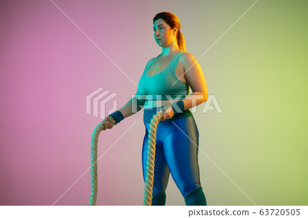 Young caucasian plus size female model's training on gradient purple green background Young caucasian plus size female model's training on gradient purple green background 63720505