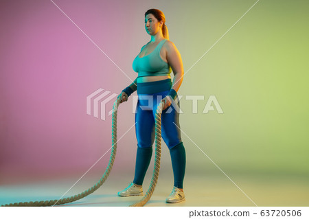 Young caucasian plus size female model's training on gradient purple green background Young caucasian plus size female model's training on gradient purple green background 63720506