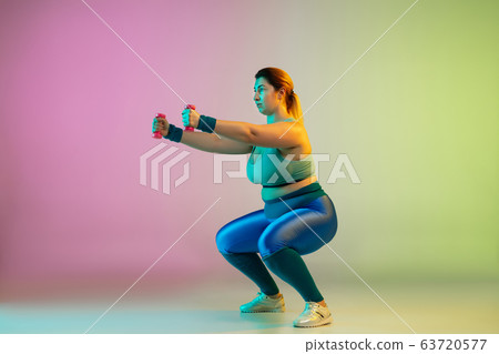 Young caucasian plus size female model's training on gradient purple green background Young caucasian plus size female model's training on gradient purple green background 63720577