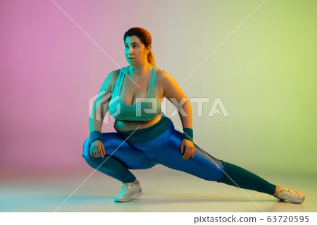 Young caucasian plus size female model's training on gradient purple green background Young caucasian plus size female model's training on gradient purple green background 63720595
