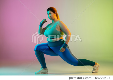 Young caucasian plus size female model's training on gradient purple green background Young caucasian plus size female model's training on gradient purple green background 63720597