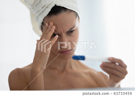 Closeup frustrated by negative pregnancy test result woman in bathroom 63733459