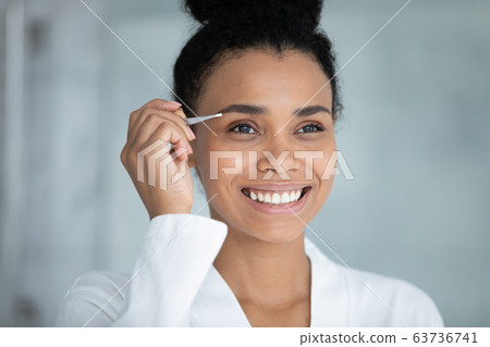 African beautiful woman tweezing eyebrows with tweezers African beautiful woman tweezing eyebrows with tweezers 63736741