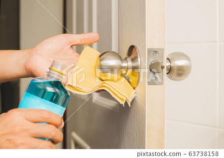 Hand cleaning door knob with alcohol and yellow microfiber cloth. 63738158