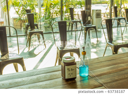 Social distancing, alcohol gel and tip box on table with empty chairs. Social distancing, alcohol gel and tip box on table with empty chairs. 63738187