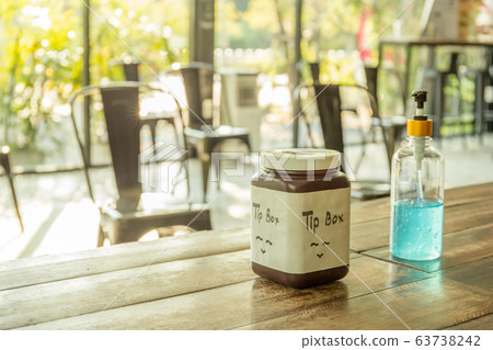 Social distancing, alcohol gel and tip box on table with empty chairs. 63738242