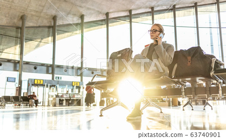 Casual blond young woman using her cell phone while waiting to board a plane at airport departure gates. Casual blond young woman using her cell phone while waiting to board a plane at airport departure gates. 63740901