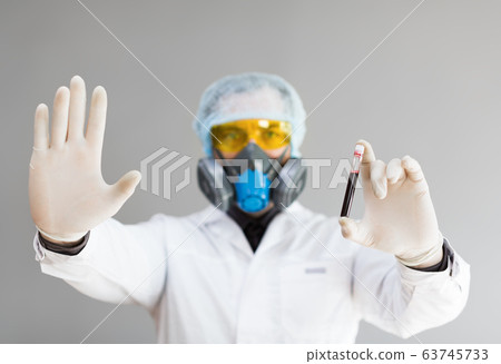 Photo of a doctor in protective clothing holds a test tube with a sample of infected blood in his hand and showing stop sign by another hand. 63745733