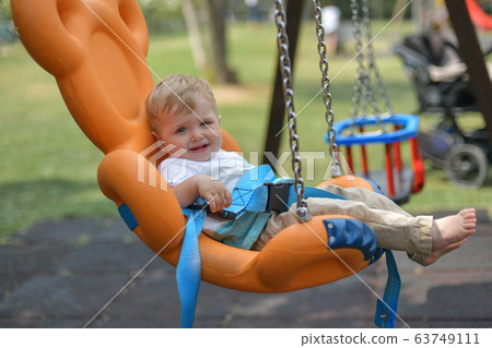 Smiling baby boy sitting in a orange swing Smiling baby boy sitting in a orange swing 63749111