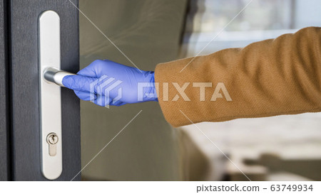 A hand in a protective glove on the handle of the front door. Protections in the midst of an epidemic A hand in a protective glove on the handle of the front door. Protections in the midst of an epidemic 63749934