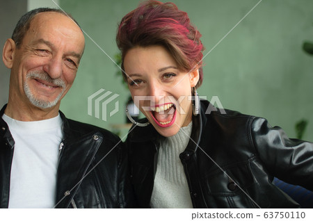 Indoor family portrait of adult daughter and senior father in loft room with houseplants. Crazy man and girl with pink hair are wearing black leather jackets in punk style and smiling Indoor family portrait of adult daughter and senior father in loft room with houseplants. Crazy man and girl with pink hair are wearing black leather jackets in punk style and smiling 63750110
