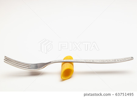 Penne pasta on the fork on the white table. Penne pasta on the fork on the white table. 63751495