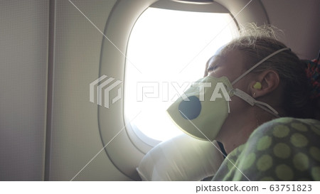 Woman travel caucasian at plane with wearing protective medical mask. Girl tourist at aircraft with respirator, feel bad and sleeps. 63751823